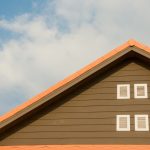 Modern house facade featuring orange roof and shuttered windows against a bright blue sky.